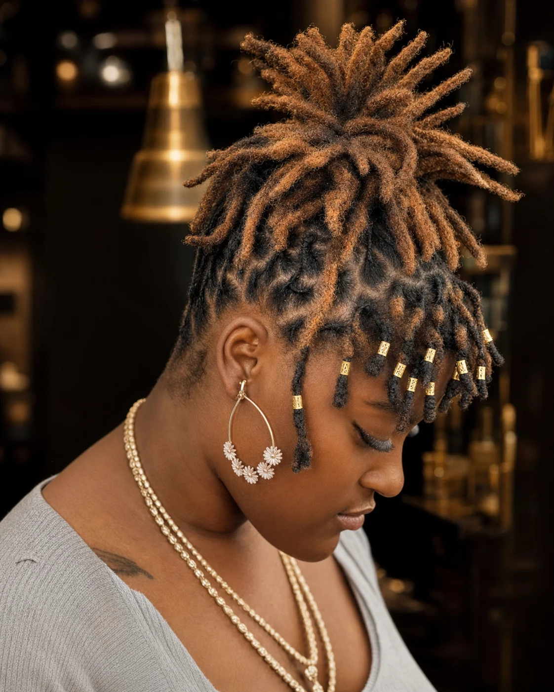 Short warm-tipped locs styled upward with gold cuffs and a clean side fade